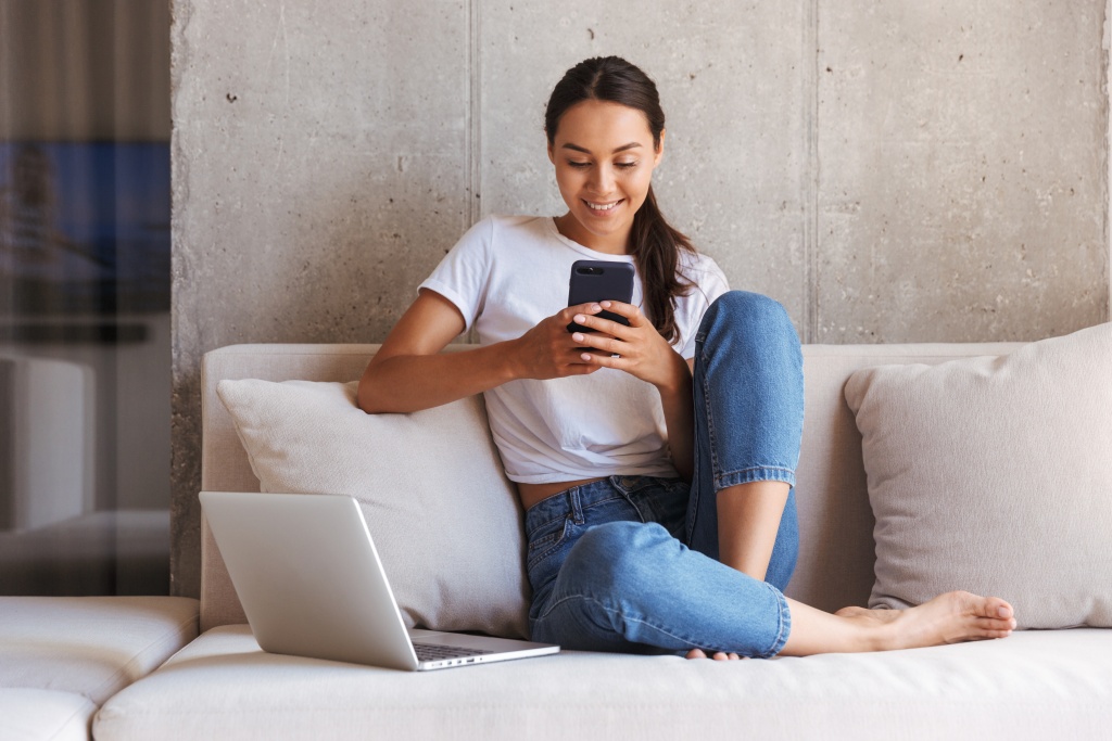 Image shows a lady sat on her phone, smiling, in a brightly lit natural room